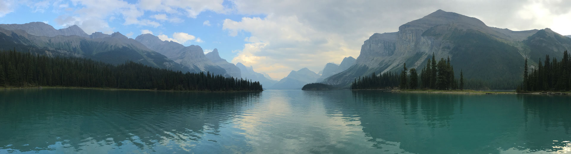 A large blue lake surrounded by evergreen trees and mountains on the horizon
